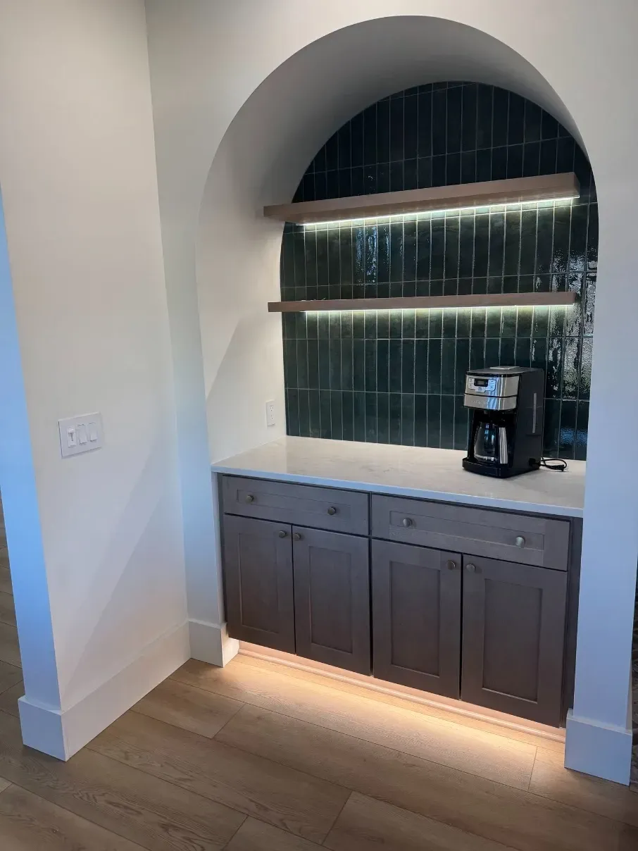 Built-in arched alcove with dark cabinets, marble counter, backlit shelves, and a coffee maker