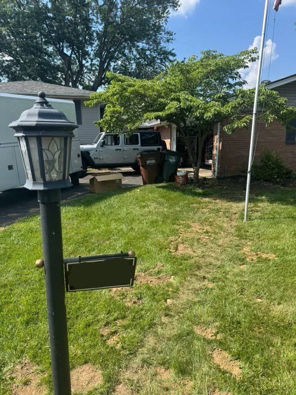 Front yard with black post lantern, grassy lawn, pickup truck, and brick house under trees
