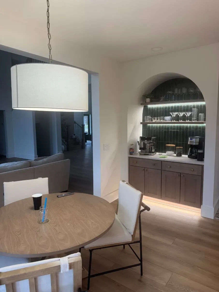 Modern dining room with round wooden table, white chairs, large pendant lamp, and arched built-in cabinet