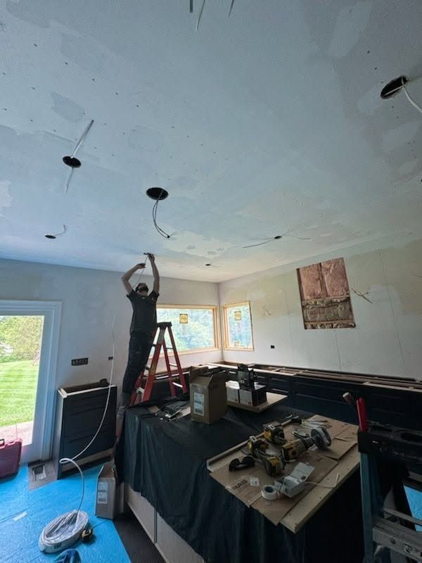 Person on a ladder installing ceiling lights in a room under renovation.