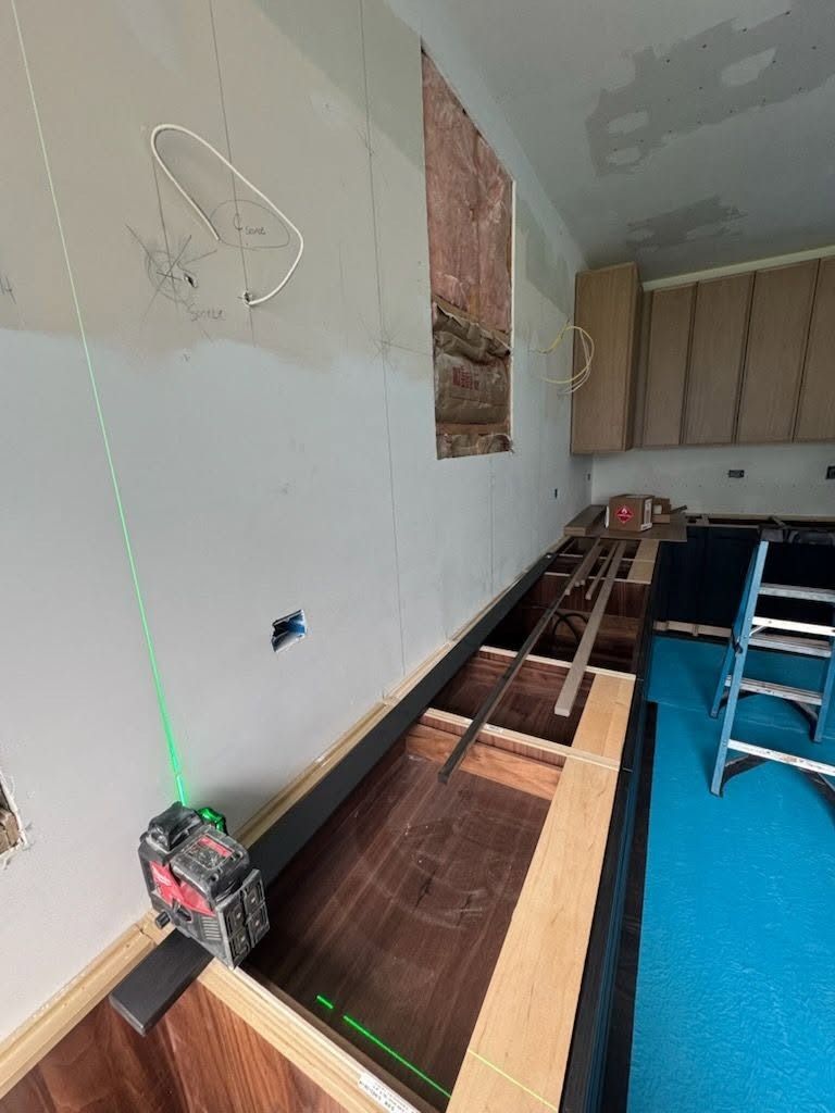 Kitchen renovation with exposed cabinet frames, green laser level, and a ladder against the wall.