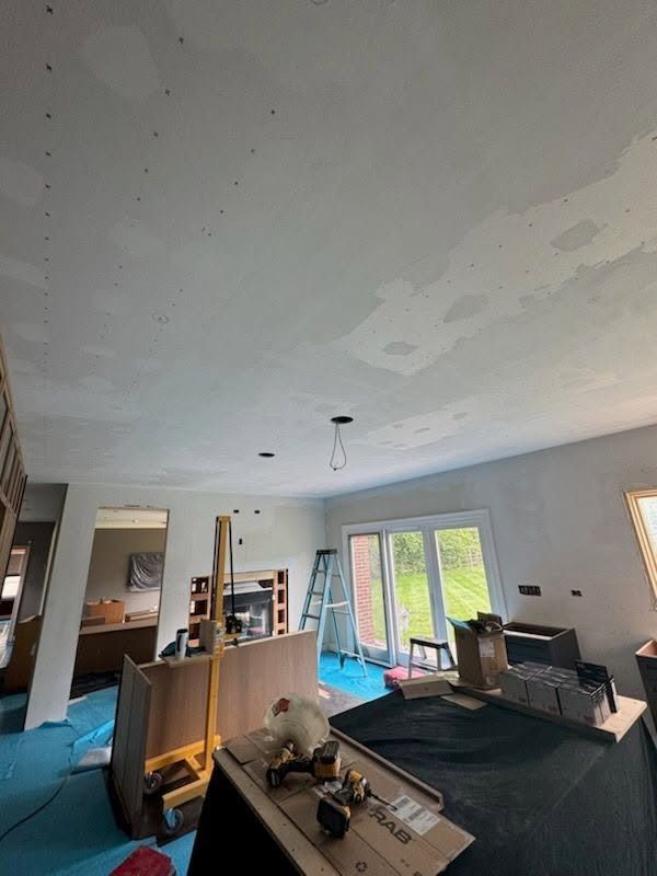 Living room under renovation with exposed ceiling, tools, and furniture on protective coverings