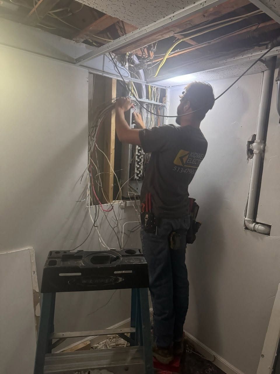 Worker adjusting exposed ceiling wiring in a narrow hallway during renovation