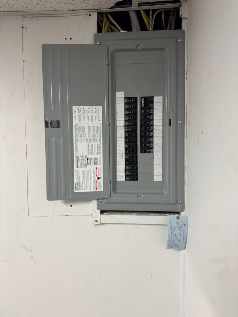 Open electrical breaker panel with gray metal doors in a white wall.