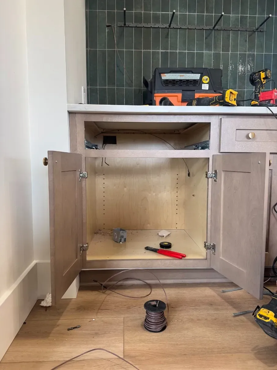Open kitchen cabinet with tools inside and on the counter, in a home renovation setting