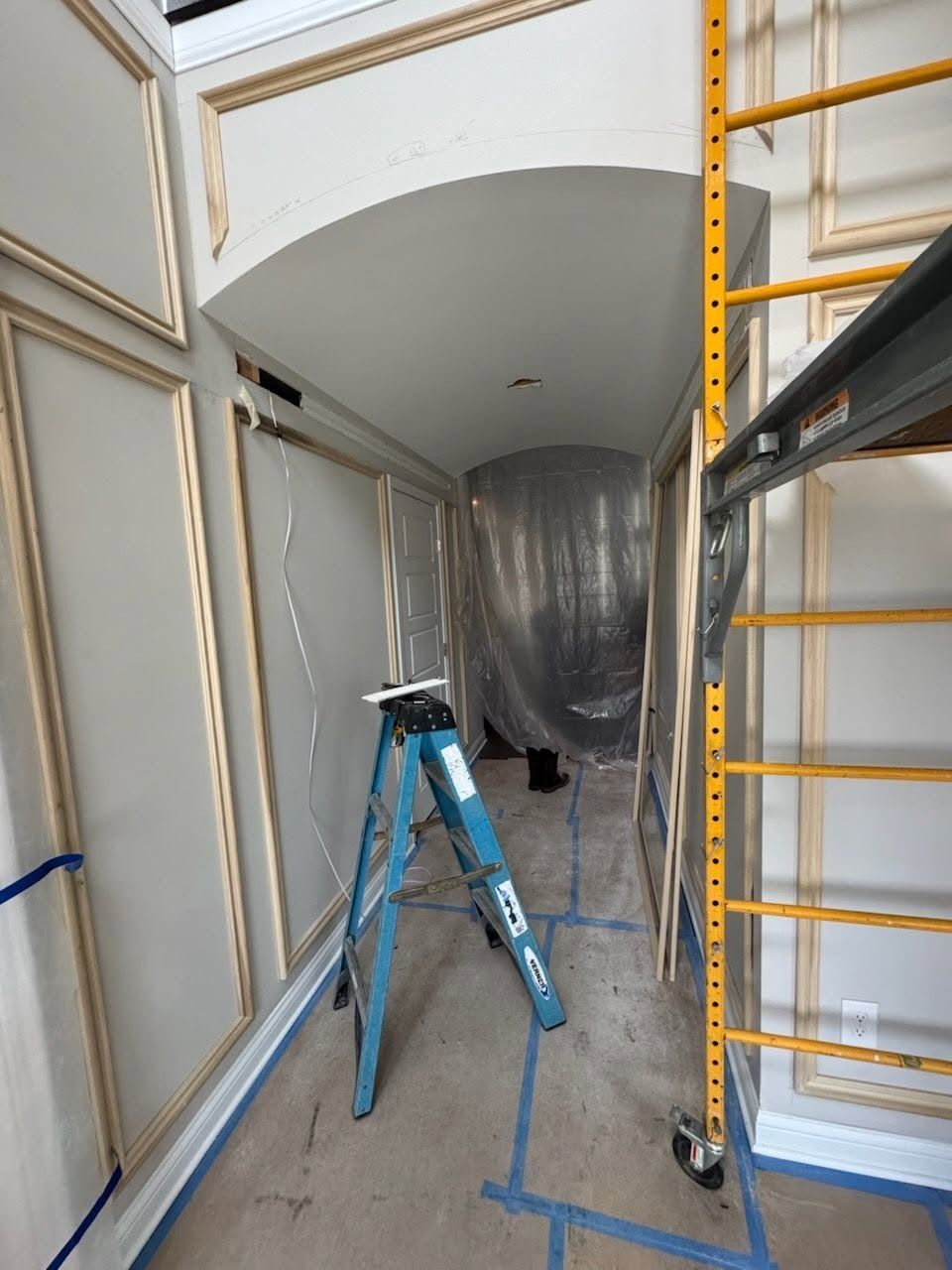 Unfinished hallway with scaffolding, ladder, and plastic-covered doorway during renovation