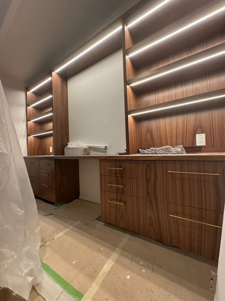 Built-in wooden display shelves and cabinets in a room under renovation, with protective floor covering.