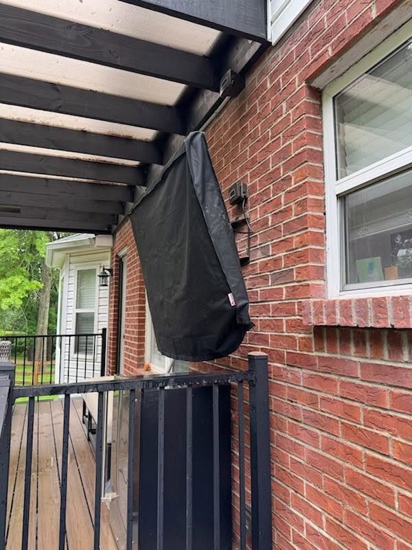 Covered porch with black railing and brick wall, showing a black hanging cover beside a window.