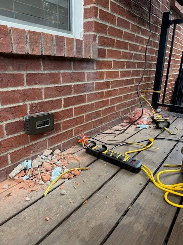 Outdoor deck beside brick wall with exposed damaged siding, tools, and debris from repairs