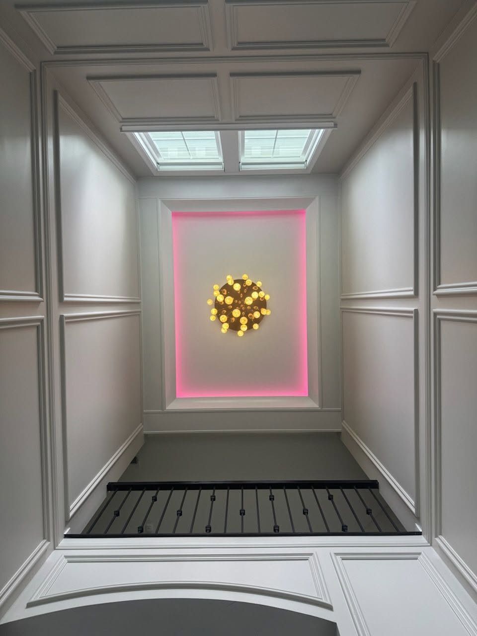 White paneled hallway with pink-lit doorway and a glowing gold wreath centered on the far wall.