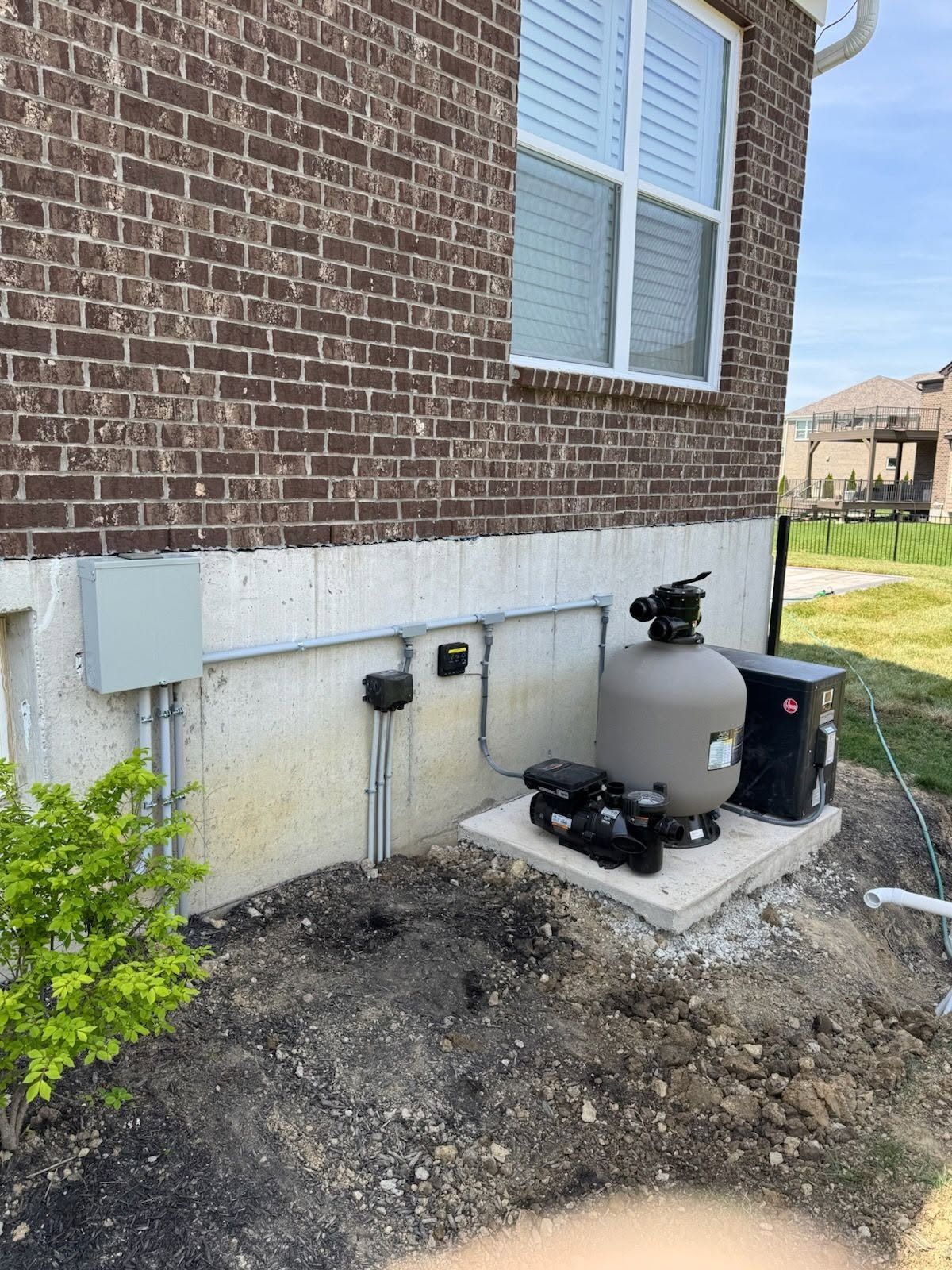 Exterior of brick house with gas meters, utility boxes, and a small shrub beside the foundation