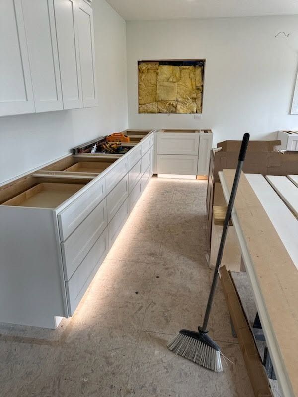 Partially renovated kitchen with white cabinets, long countertop, and a broom on the floor