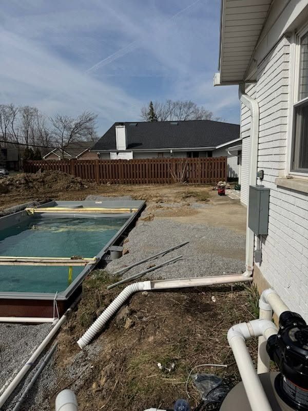 Backyard with an above-ground pool, white house siding, and a gravel patio under a clear sky