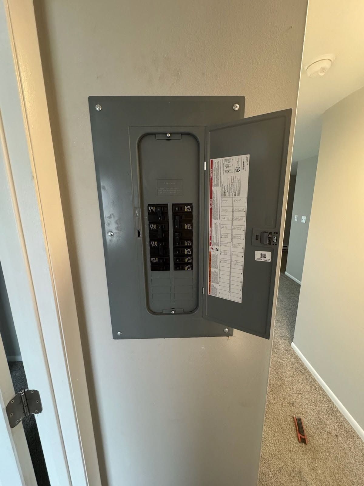 Open electrical breaker panel in a hallway with the door ajar