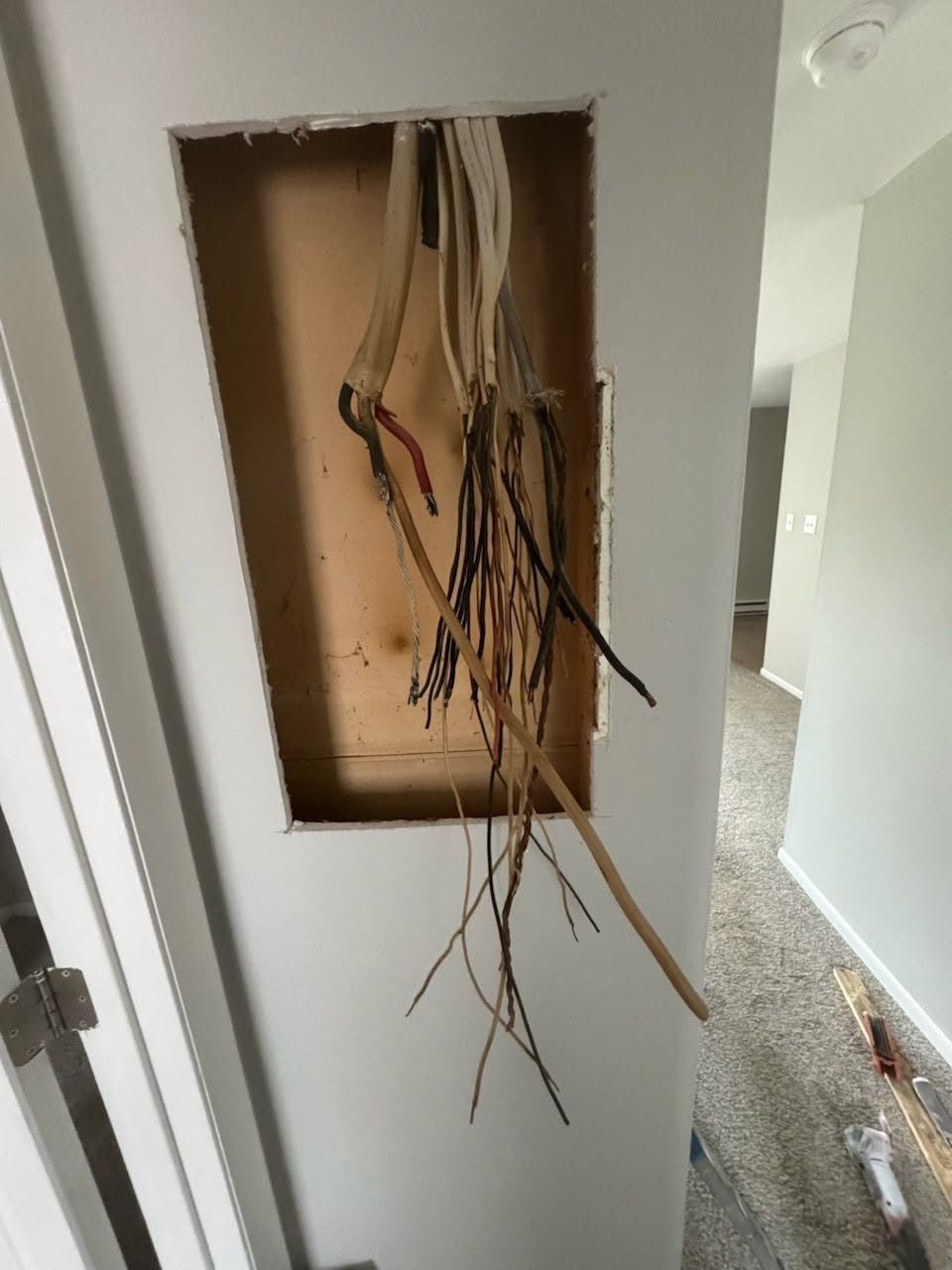 Open wall cavity with exposed electrical wires hanging out near a doorway
