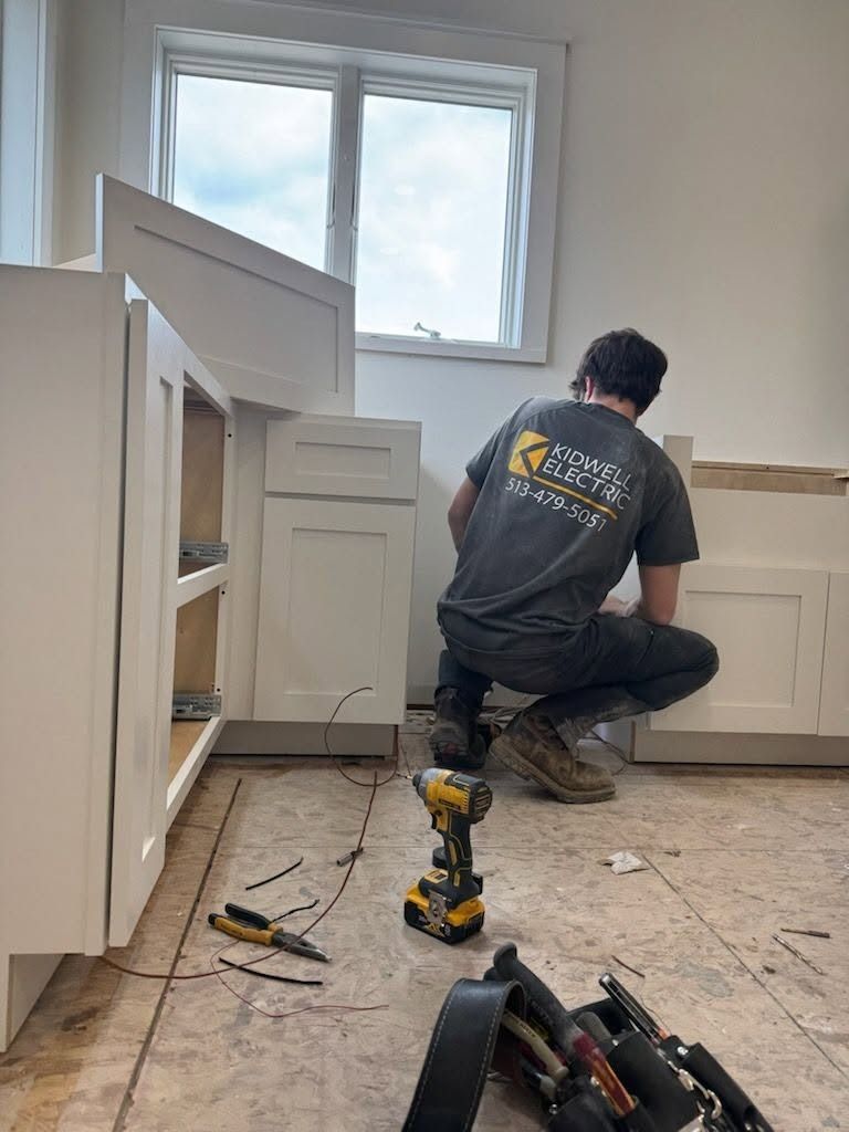 Person kneeling in a kitchen installing a cabinet under a window, with tools on the floor.