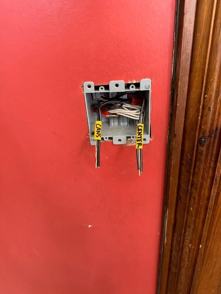 Open electrical switch box with exposed wiring on a red wall near a wooden doorframe
