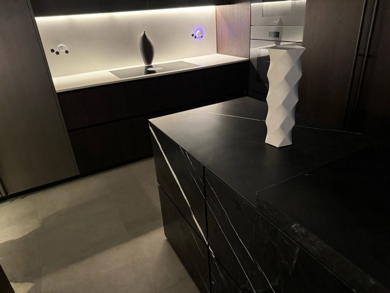 Modern kitchen with black island, white vase, and lit backsplash countertop