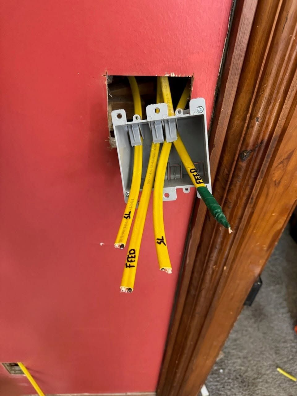 Open electrical box in red wall with yellow wires hanging out beside a wooden door frame