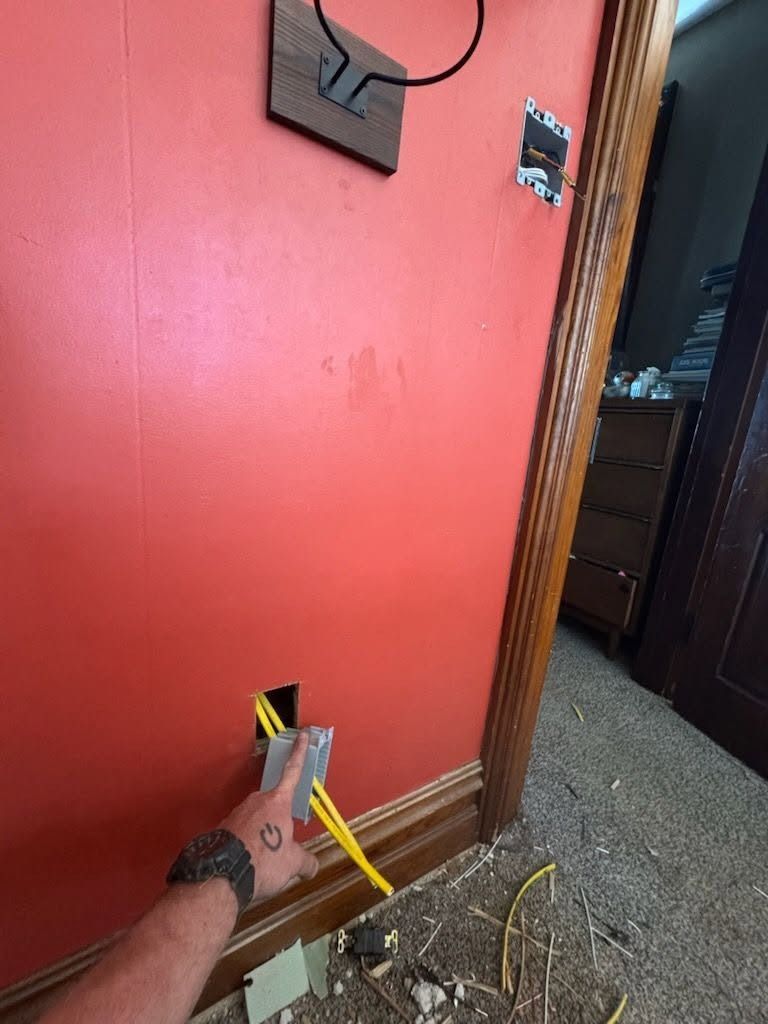 Person installing an outlet in a red wall beside a doorway, with tools and exposed wiring on the floor.