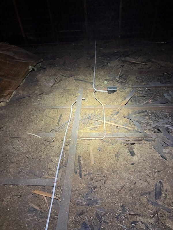 Dim attic floor with insulation, loose wires, and a flashlight beam illuminating the center.
