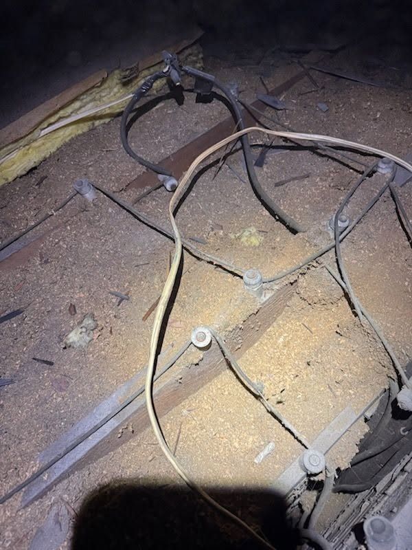 Exposed electrical wires and cables on a dusty floor near a wall, lit by a flashlight.