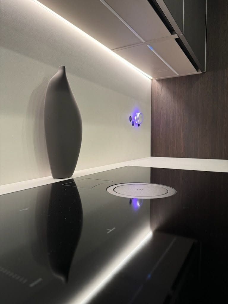 Modern kitchen counter with glossy black surface, white wall, and decorative vase under soft lighting