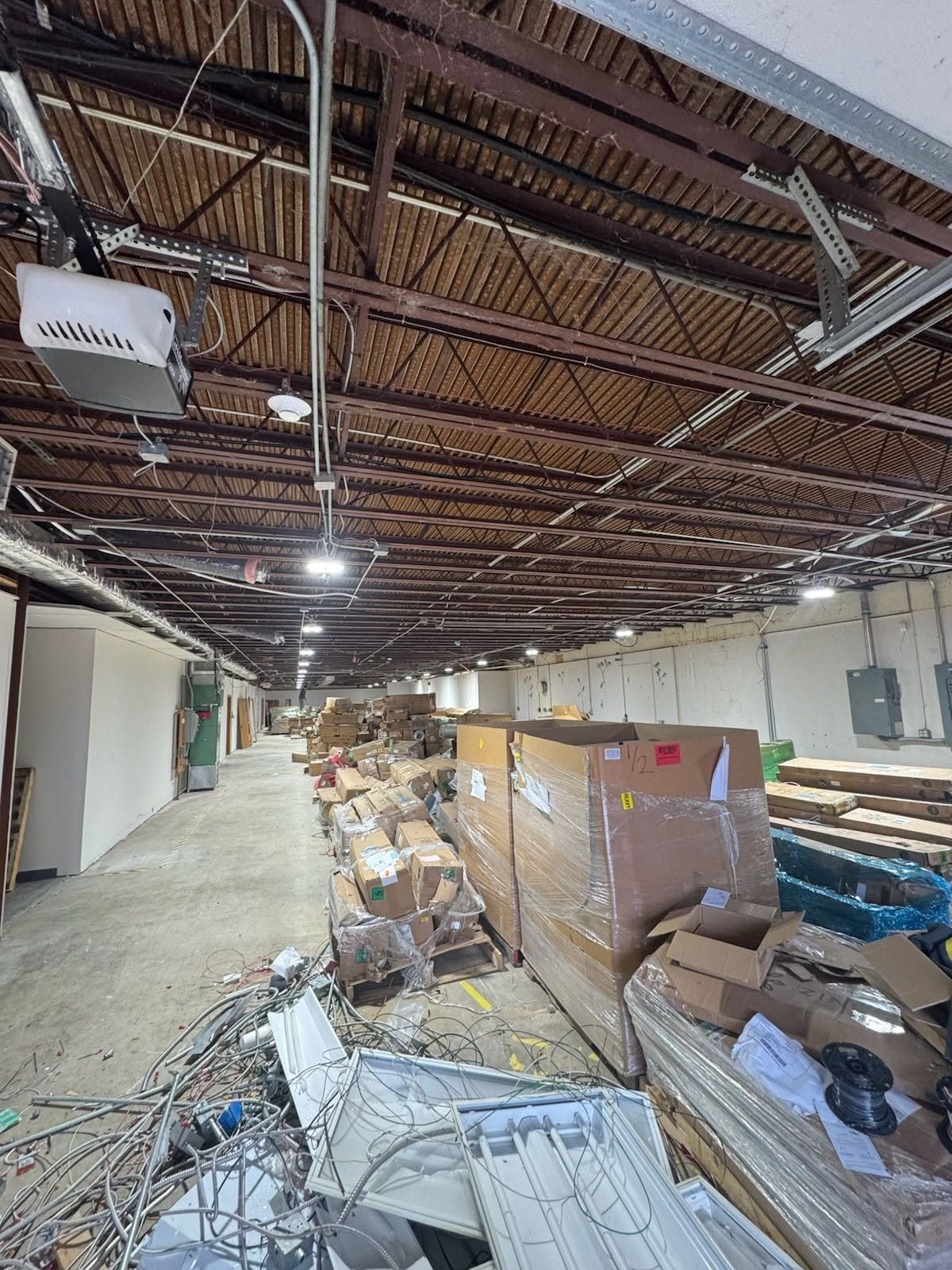 Abandoned warehouse interior with debris piles, exposed ceiling beams, and scattered cables on the floor