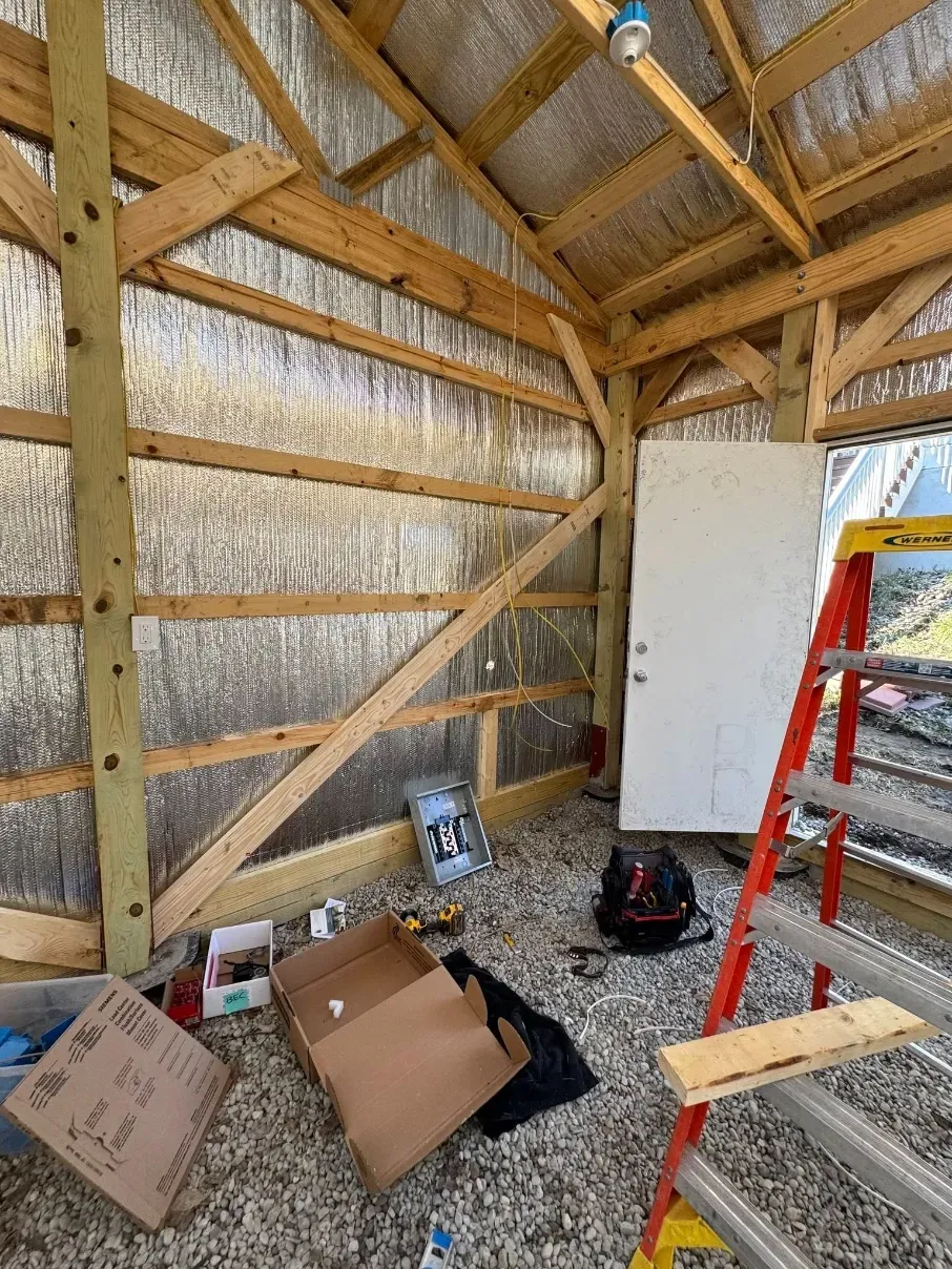 Wood-framed shed interior with insulation, boxes on the floor, and a red ladder leaning against the wall