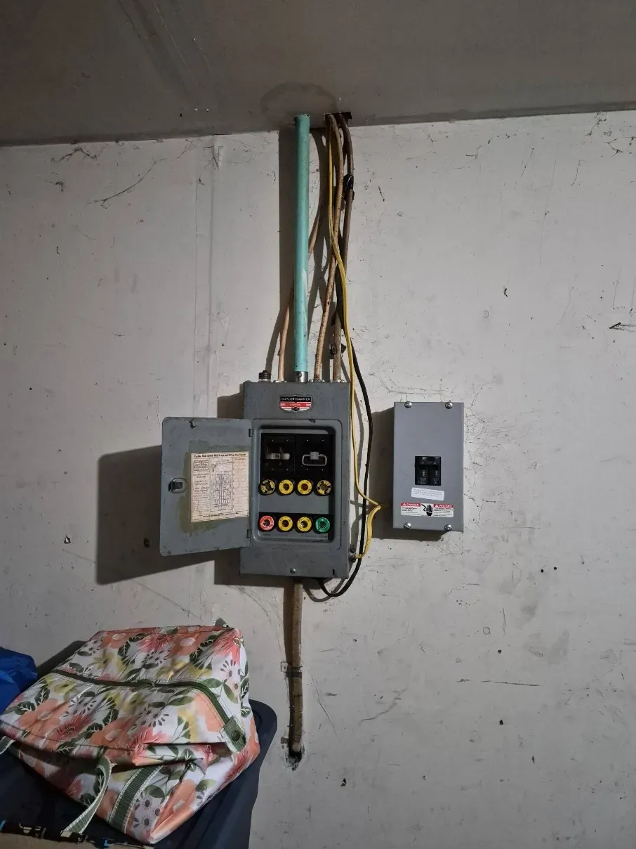 Wall-mounted electrical breaker panel with exposed wires and an open cover in a utility room