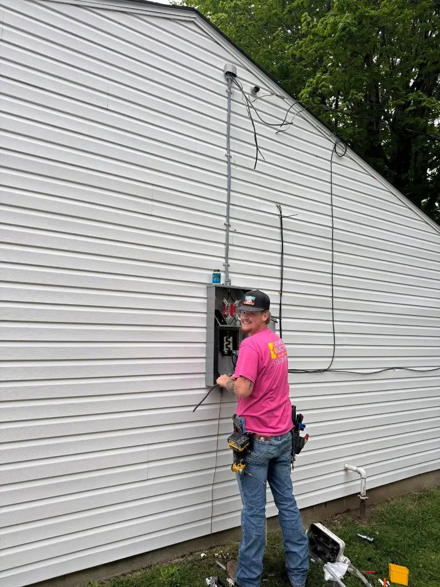 Man standing on a ladder repairing siding on a white house with a tool belt and extension cord