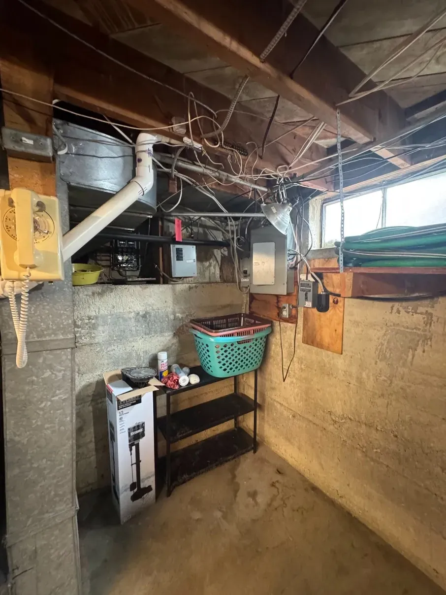 Basement utility area with exposed pipes, water heater, shelves, and a basket on a table.