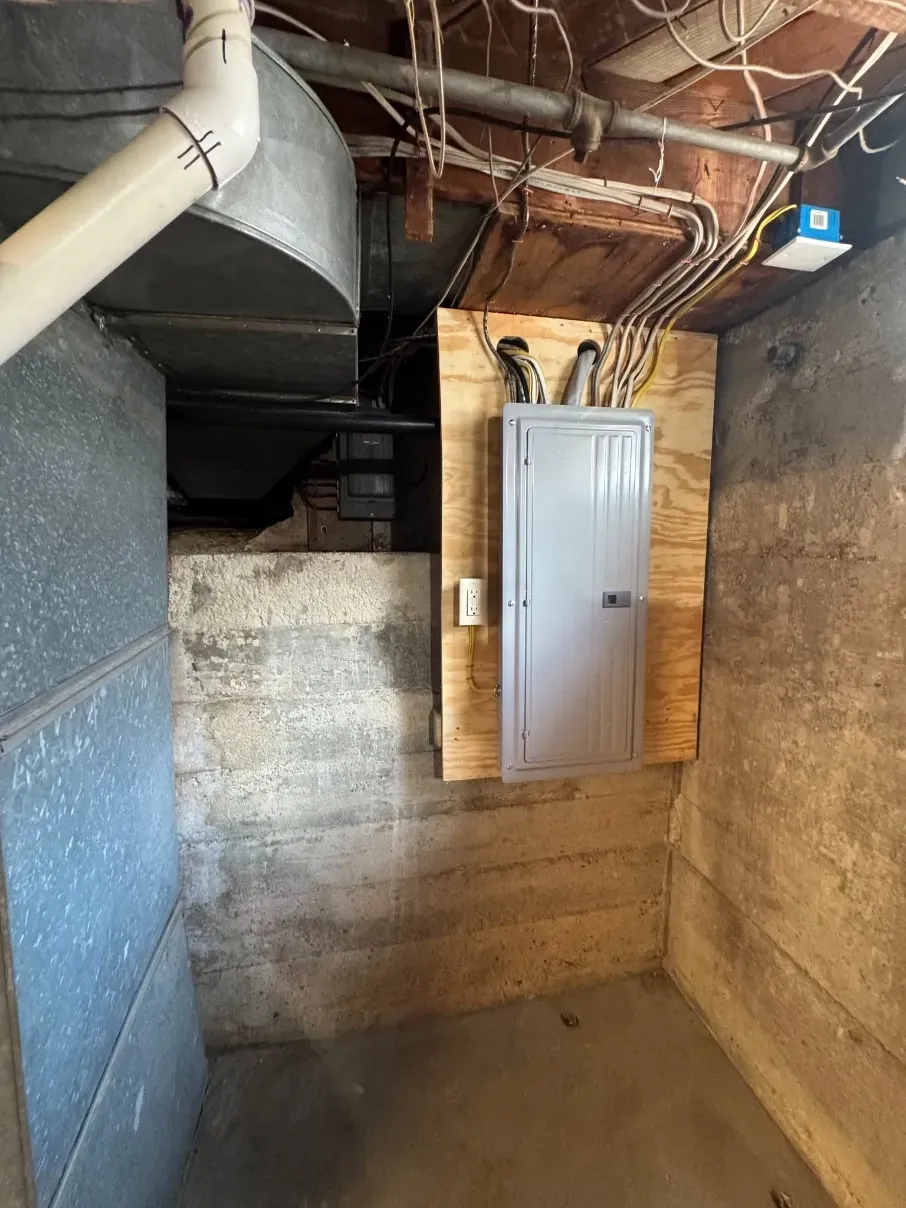 Basement utility room with furnace ductwork, concrete walls, and a gray electrical panel on wood framing