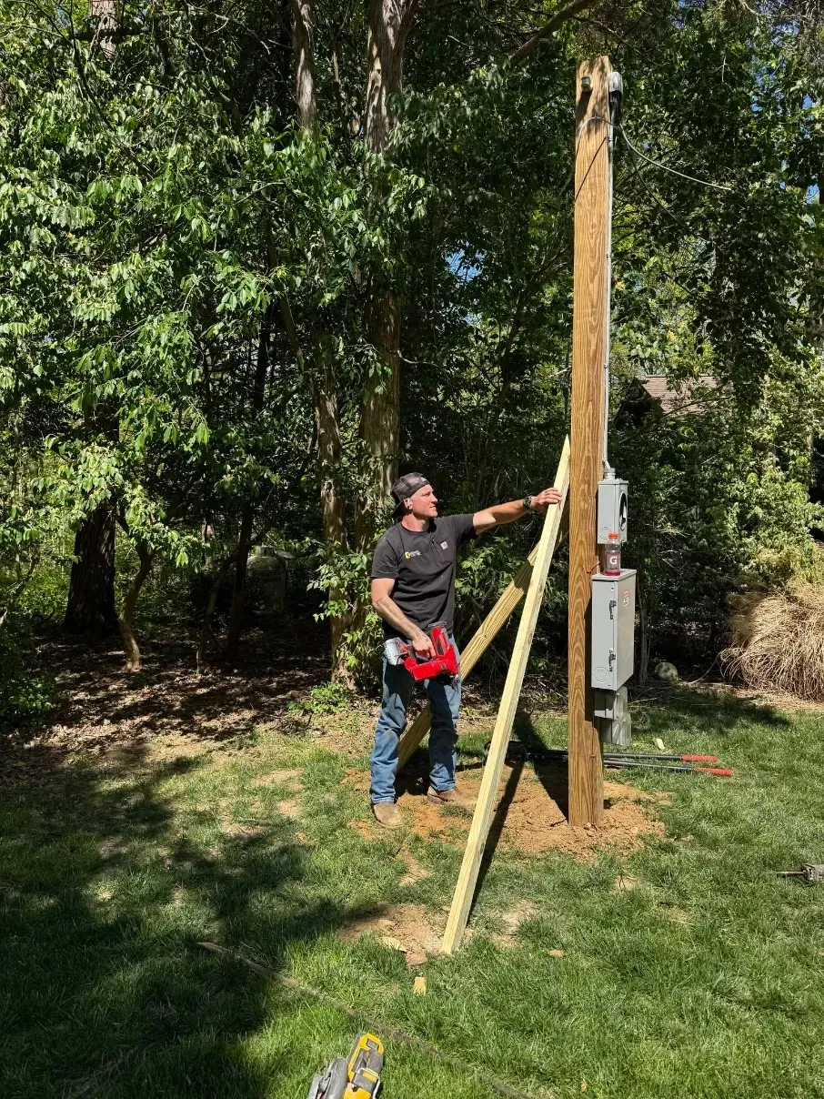 Person measuring a tall wooden post with a tape measure in a grassy wooded area