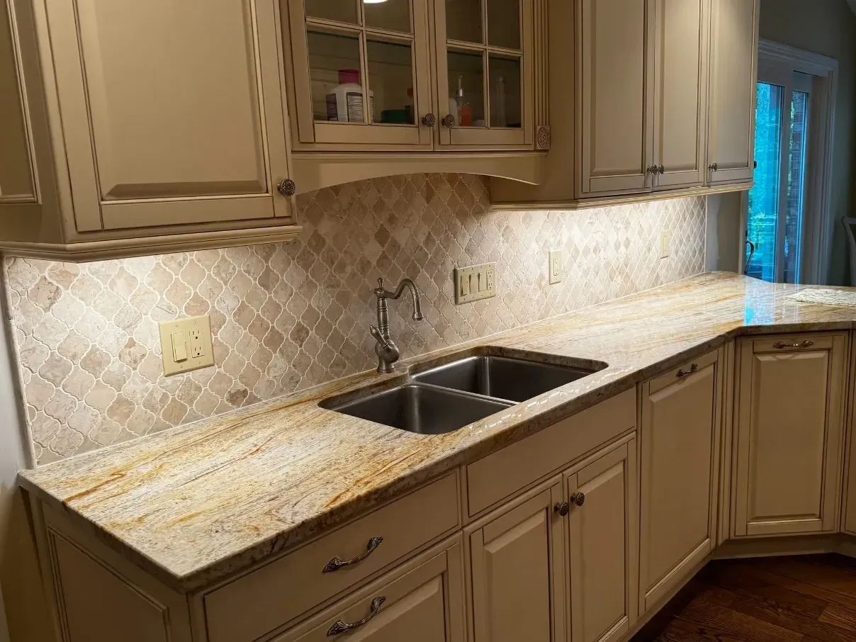 Kitchen with beige cabinets, speckled countertops, double sink, and tiled backsplash under under-cabinet lighting