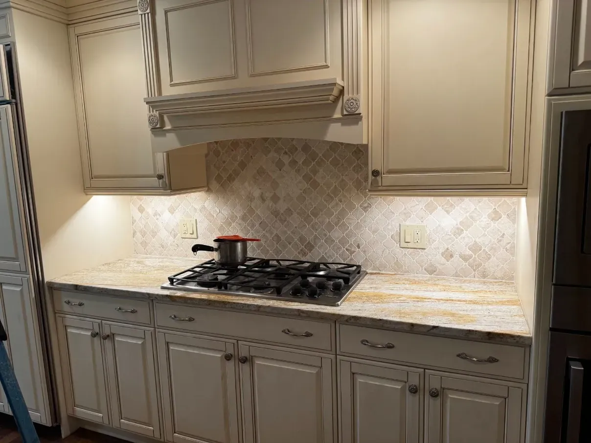 Elegant beige kitchen with built-in cabinets, patterned backsplash, and gas cooktop on a marble countertop.