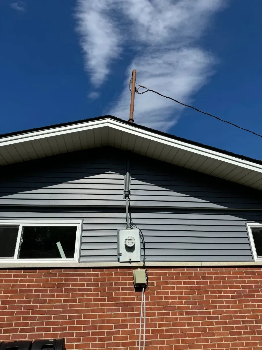 House exterior with gray siding, brick lower wall, utility meter, and blue sky above