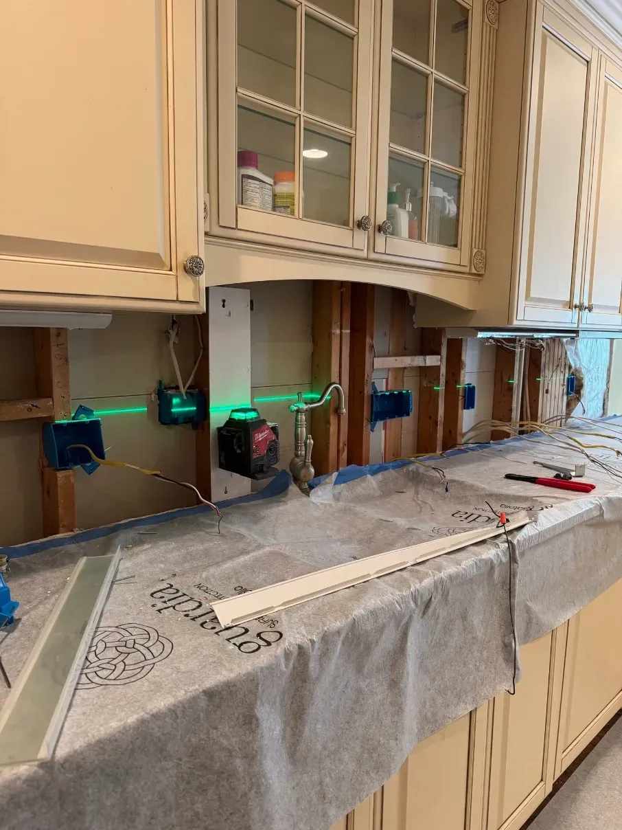 Kitchen counter with cabinets, sink, and tools laid out under an open upper cabinet.