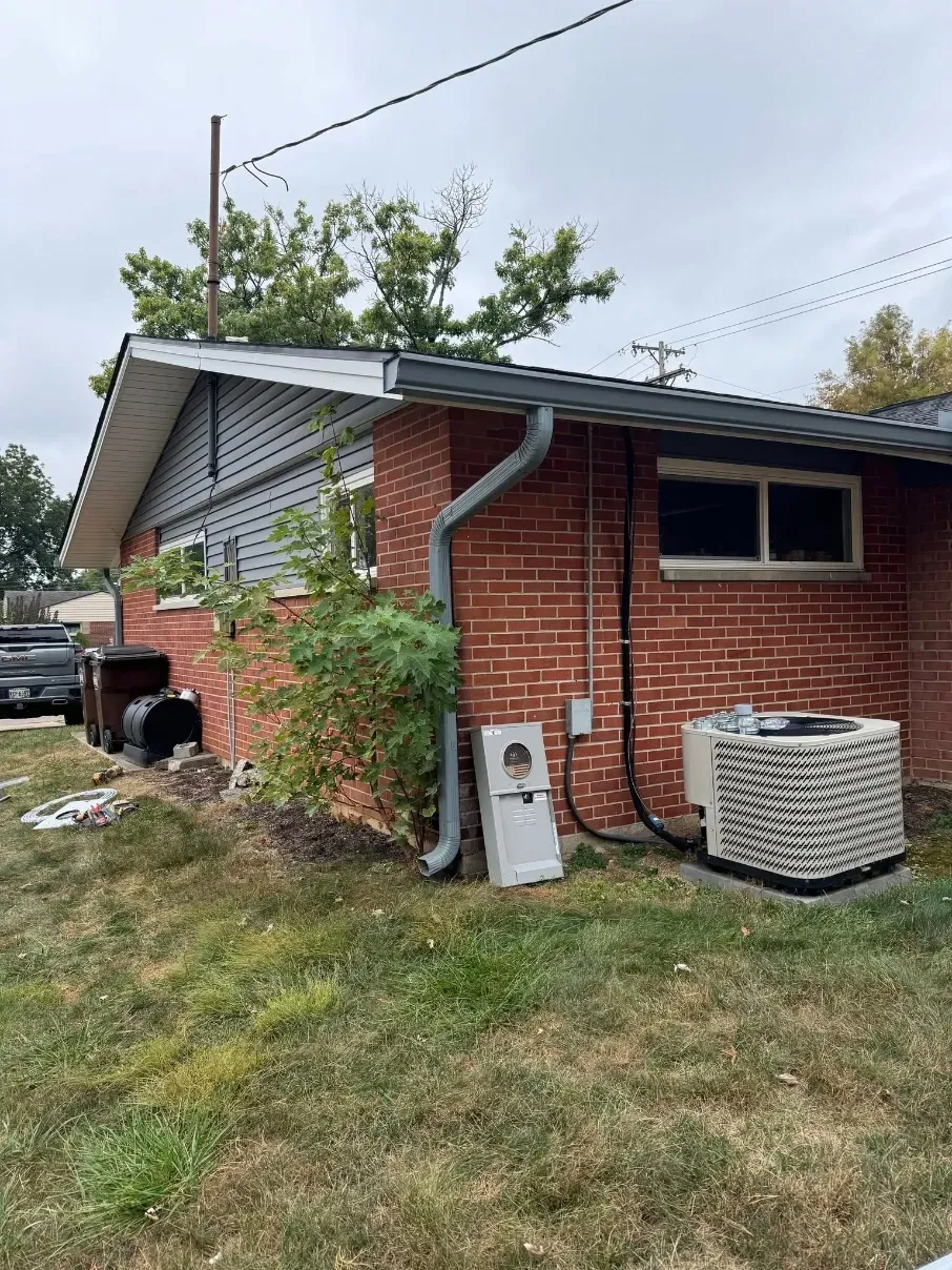 Brick house exterior with white siding, downspout, and air conditioner in a grassy yard