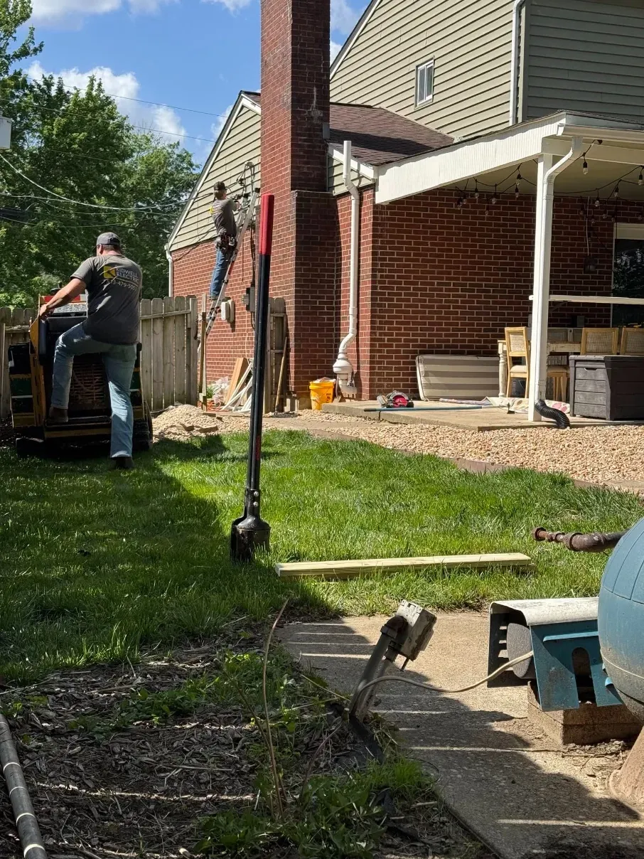 Person mowing a lawn beside a brick house on a sunny day
