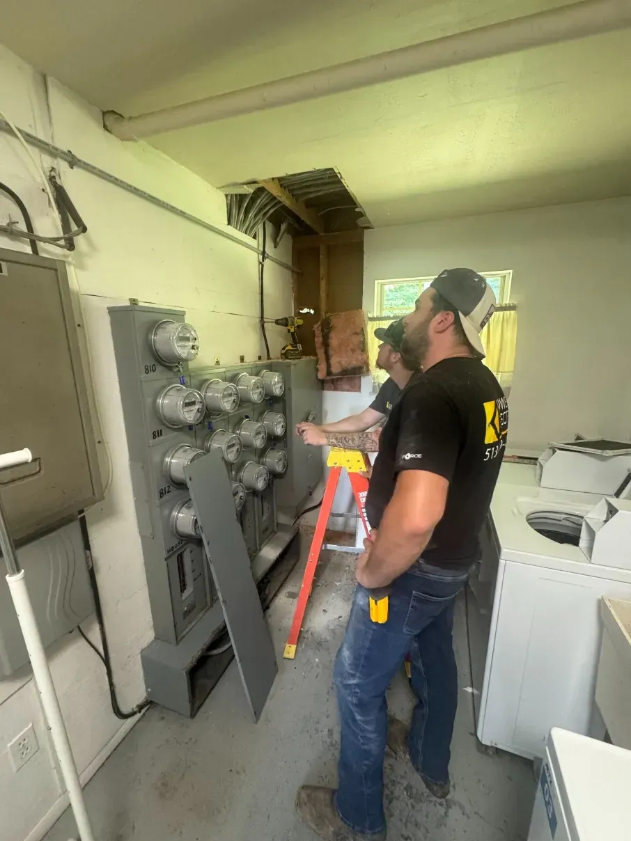 Two utility workers inspecting electrical panels in a small industrial room