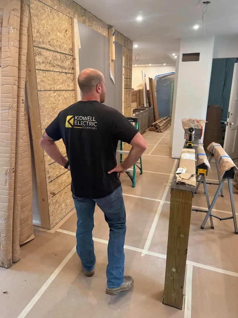 Man standing in a narrow hallway under renovation, facing drywall work and construction materials.