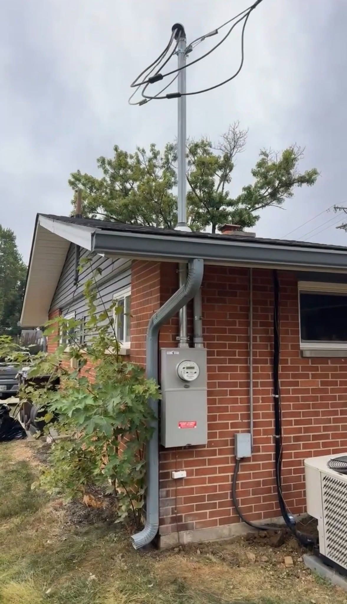 Brick utility building with power meter, gray electrical box, and overhead wires by trees.