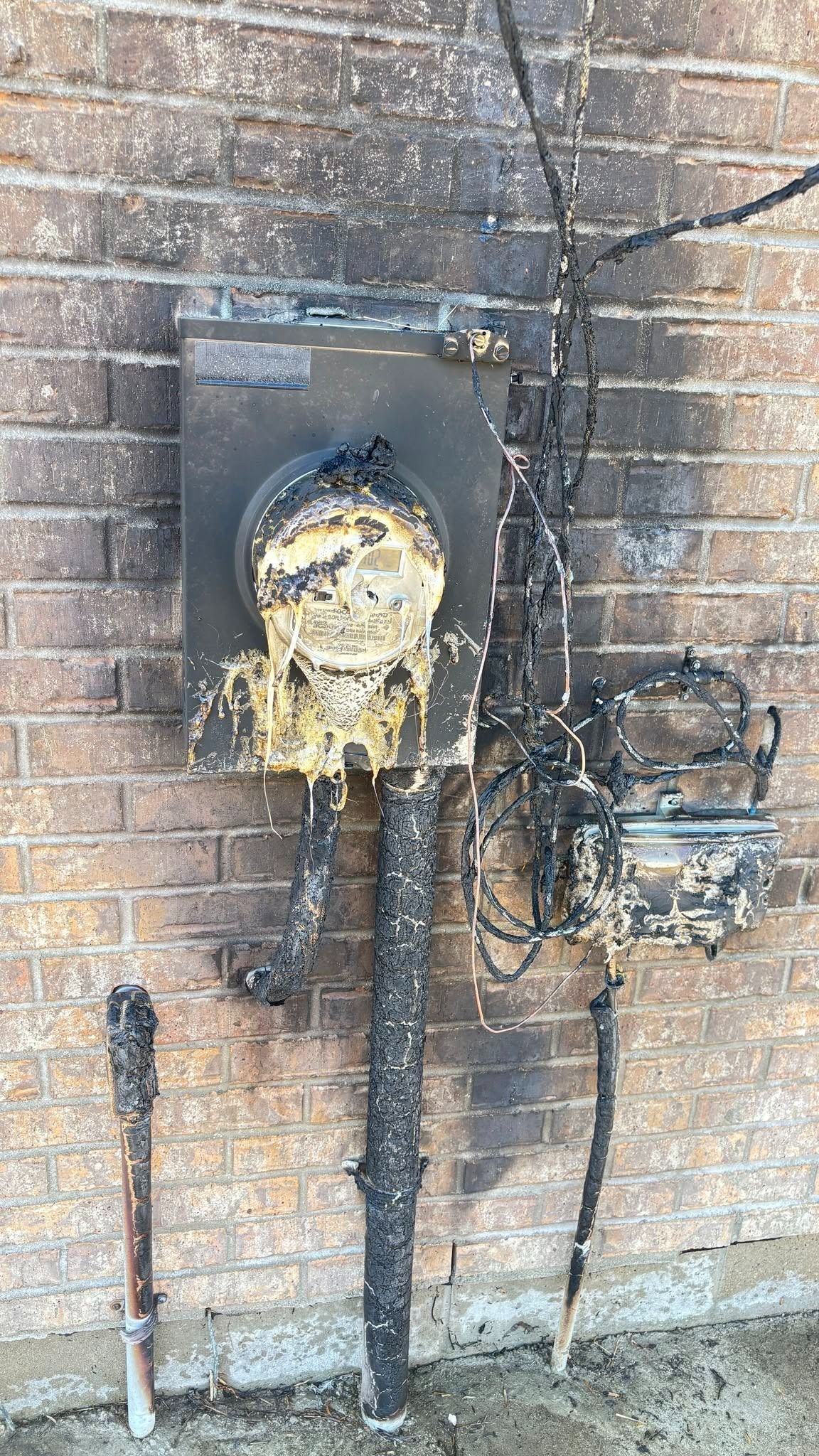Damaged brick wall with a corroded electrical meter and exposed wiring covered in debris