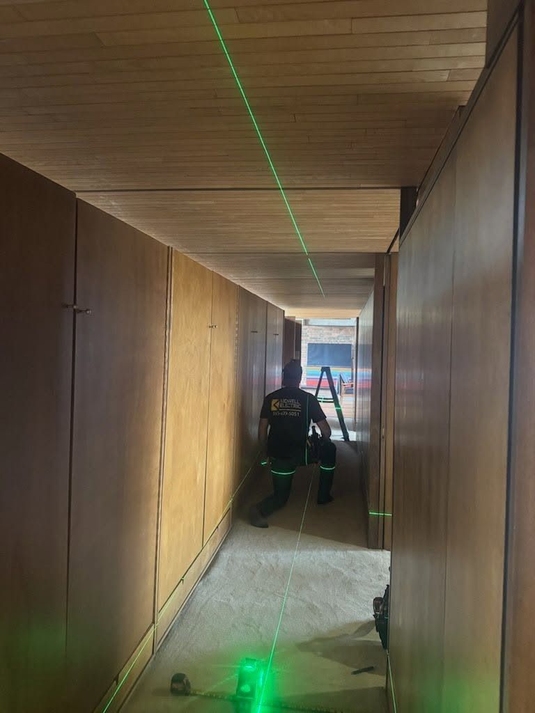 Person kneels in a narrow hallway with green laser lines on the floor and ceiling.