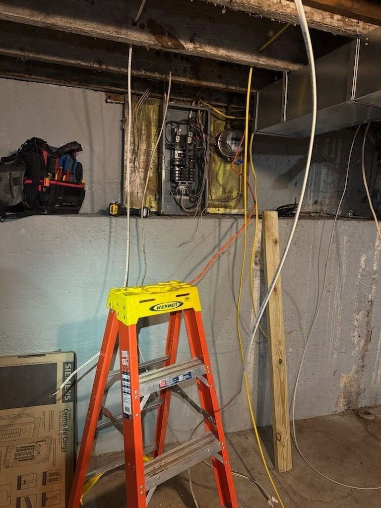 Partially finished basement with ladder, exposed wiring, and ceiling pipes under repair