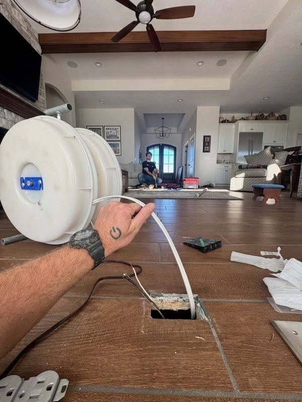 Hand holding a white cable reel on a wooden floor in a modern living room under renovation
