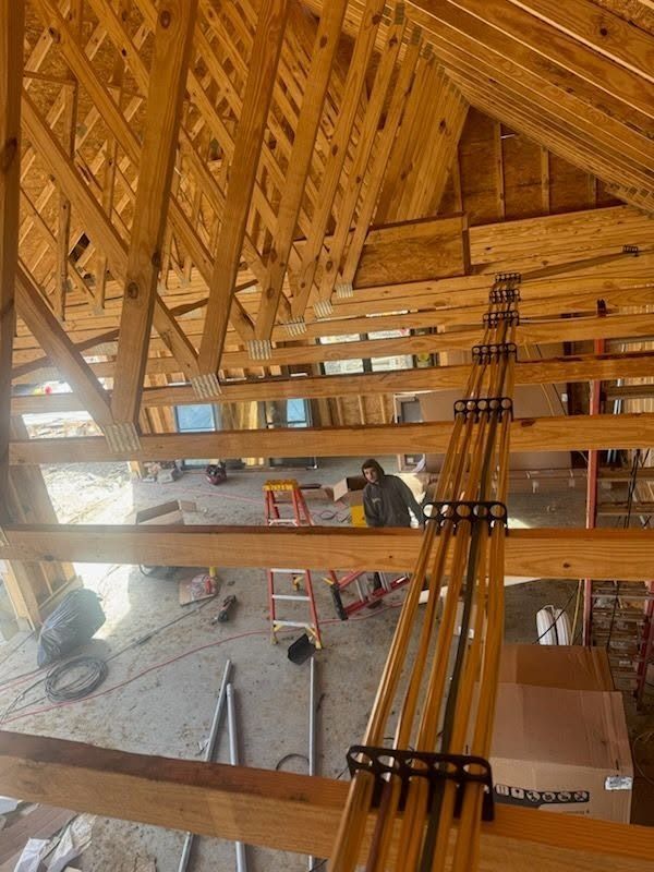 Unfinished wooden attic framing with exposed trusses, plumbing lines, and construction tools on the floor.