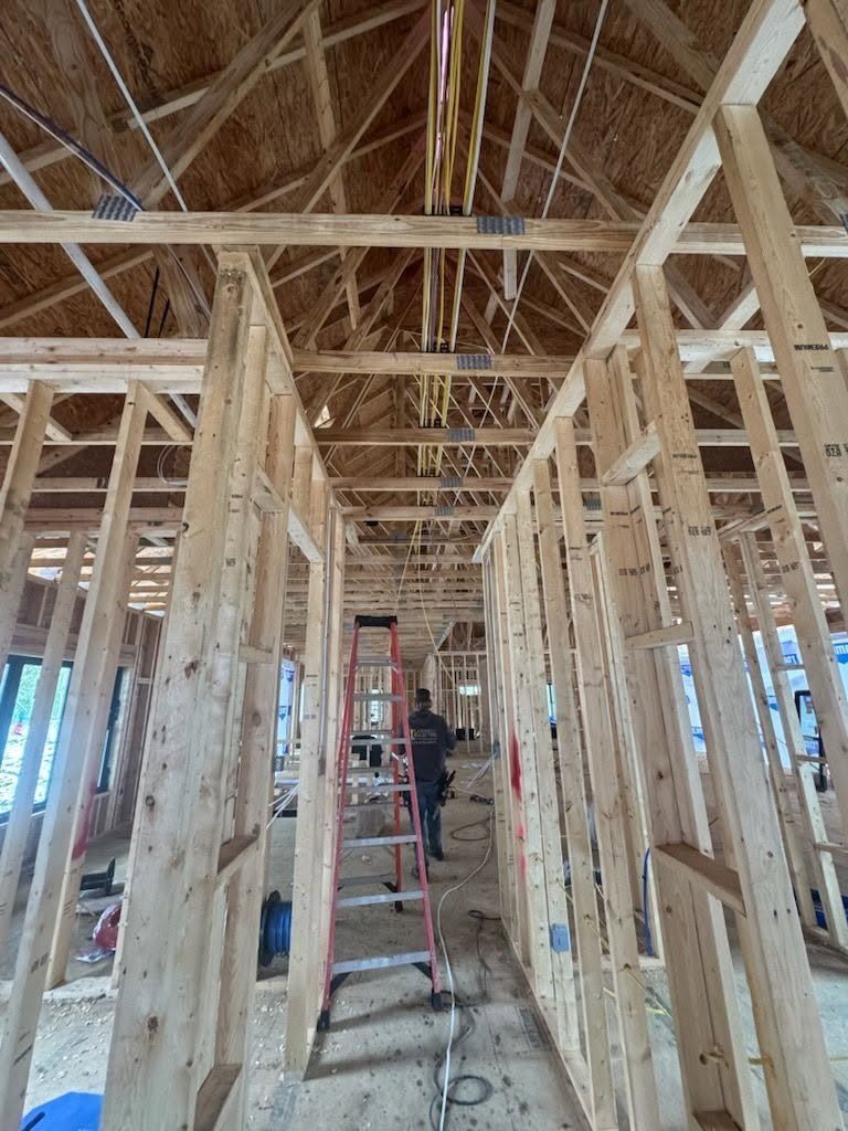 Wood-framed building interior under construction, with exposed rafters and a ladder in the center.