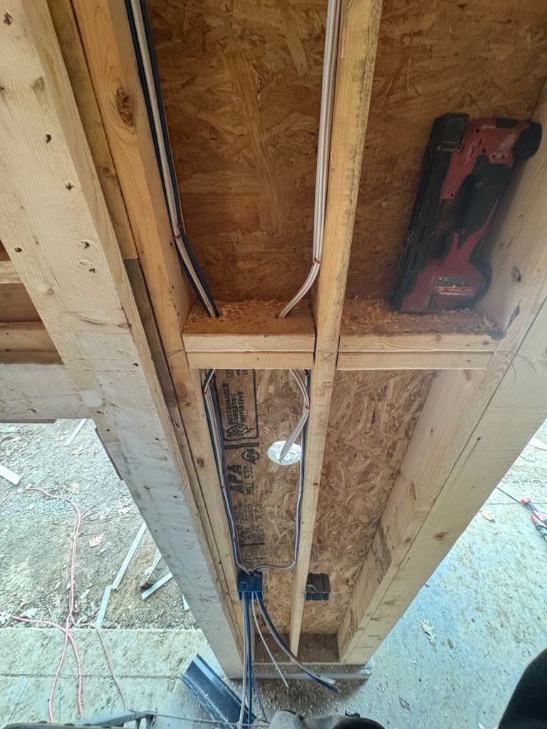 Underside of a wooden bridge or deck, showing beams, wiring, and a red tool case attached below.